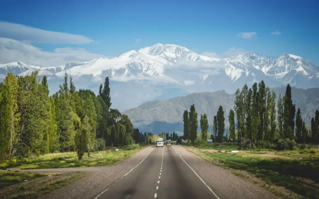 Estrada reta com vista para as montanhas da região de Mendoza, Argentina, cercada de bosques e vinhedos. As vinícolas são alguns dos melhores lugares onde ficar em Mendoza.