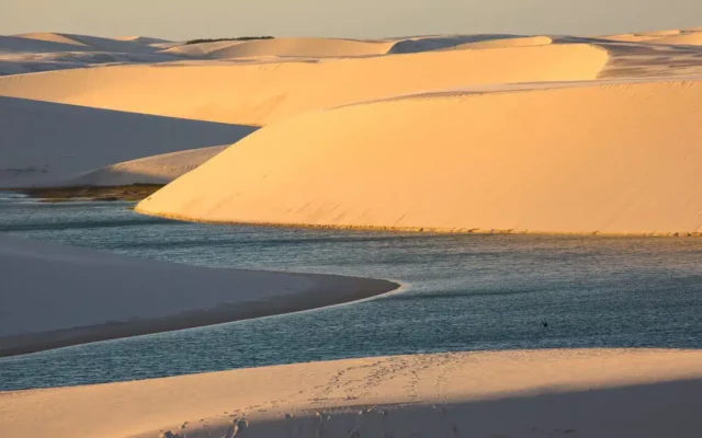 Vista dos lençóis maranhenses ao por do sol, com piscinas naturais no centro. Veja os melhores locais onde ficar em Barreirinhas para explorar o parque!