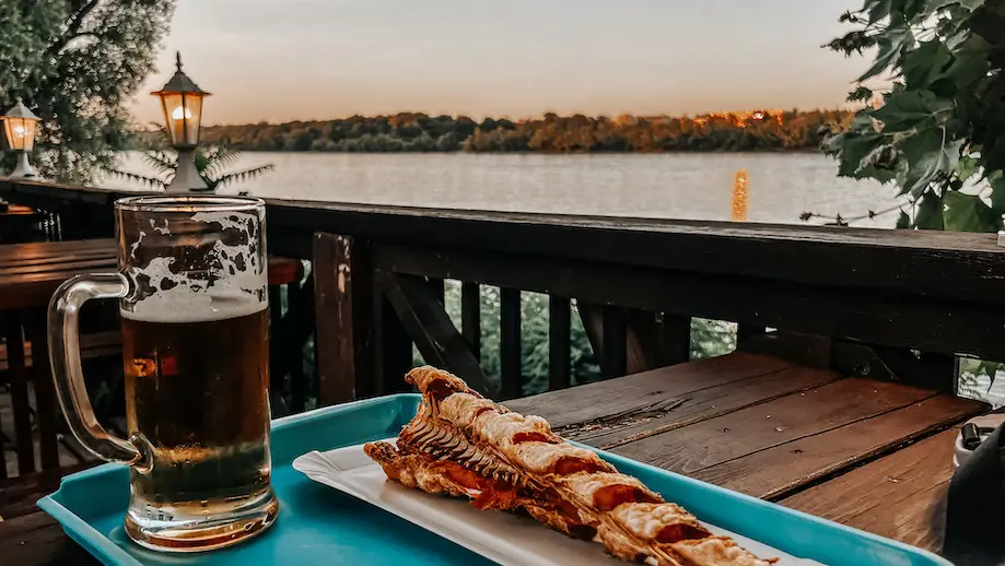 Imagem de uma cerveja com um hekk (merluza frita) em uma mesa de restaurante à beira rio na Romai Part, praia do Danúbio, em Budapeste