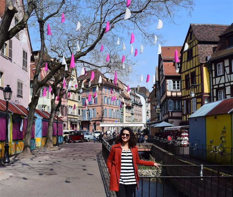 Imagem de uma mulher vestindo um casaco vermelho com blusa listrada em preto e branco em uma rua na Alsácia, França