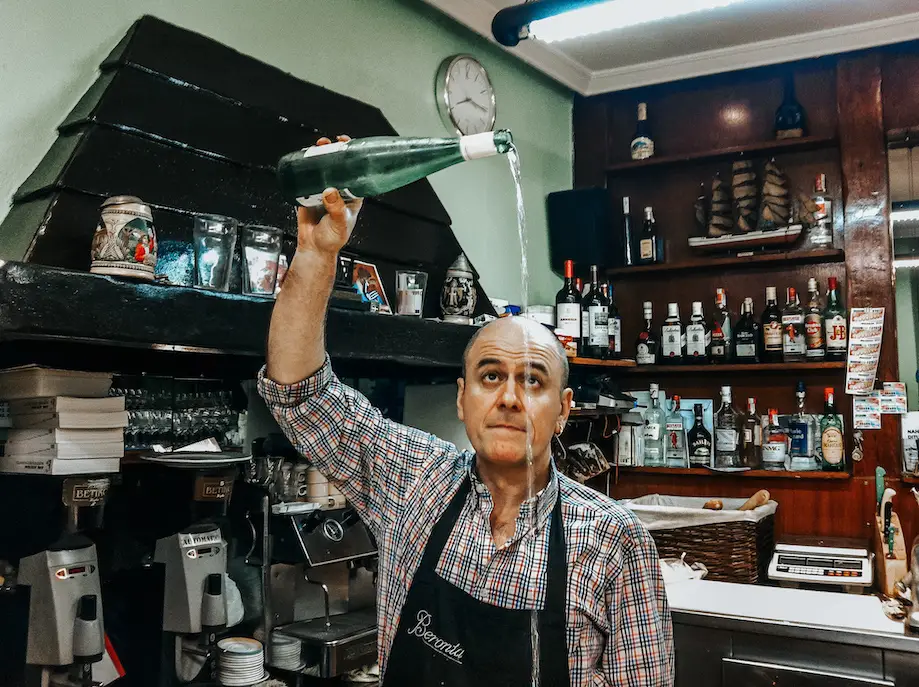 Taverneiro servindo sidra a uma longa distância da taça em uma sidreria em San Sebastián