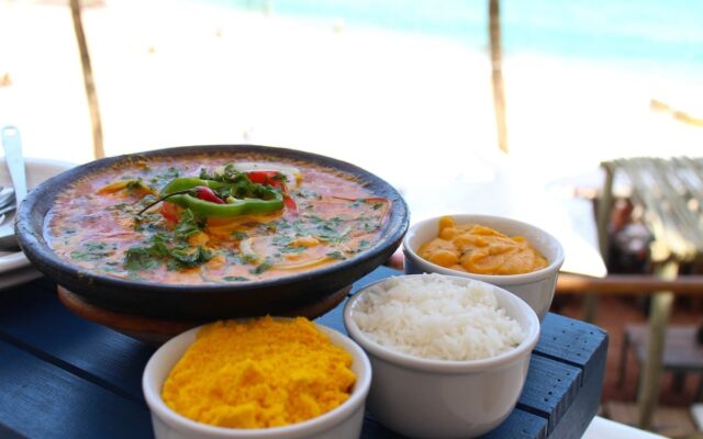 Comidas típicas do Cerá: moqueca servida em uma mesa na praia com arroz e farofa