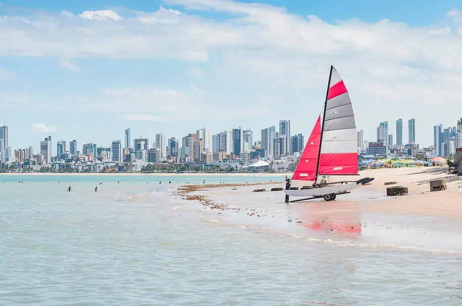 praia de João Pessoa, com cidade ao fundo e barco vermelho na areia