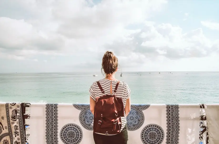Worldpackers é confiável? É seguro usar? Foto de uma menina de costas em uma varanda, olhando para o mar, de mochila vermelha nas costas
