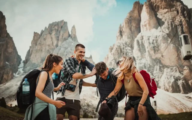Worldpackers - Voluntariado Internacional: grupo de quatro jovens com mochilas e câmeras se abraçando e rindo em frente a uma montanha