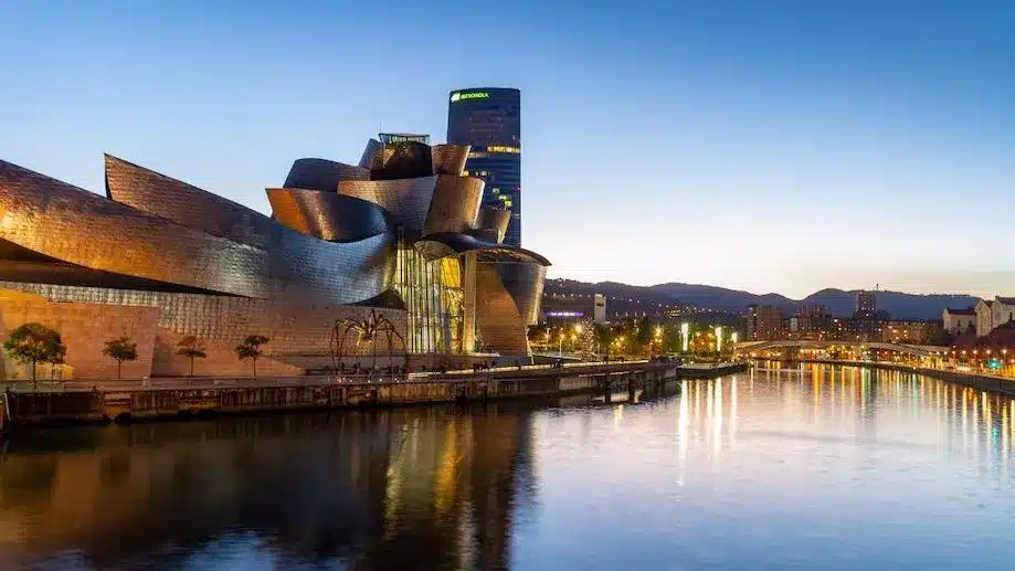 Museu Guggenhein ao entardecer, com rio ao lado. Há muitas opções de hotéis para se hospedar nessa região de Bilbao.