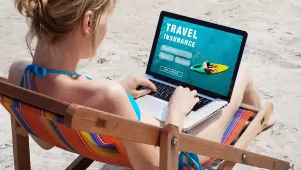 Garota com laptop na praia com página de seguro de viagem aberta 